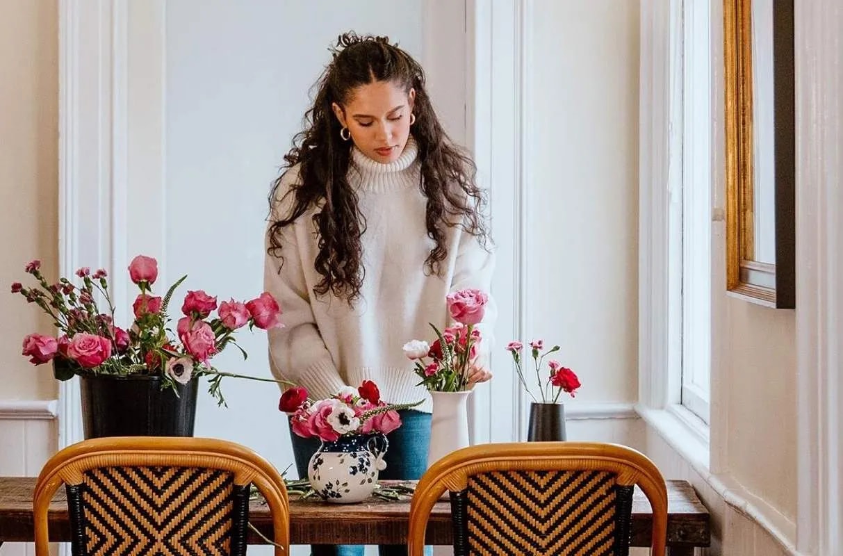 a woman arranging flowers in a vase on a table