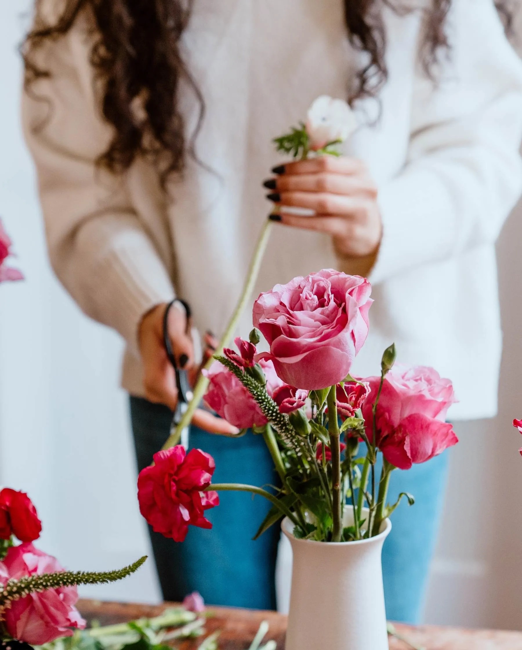 a woman arranging flowers in a vase on a table